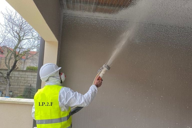 Technicien IP2F projetant un flocage coupe-feu sur un mur d'entrepôt
